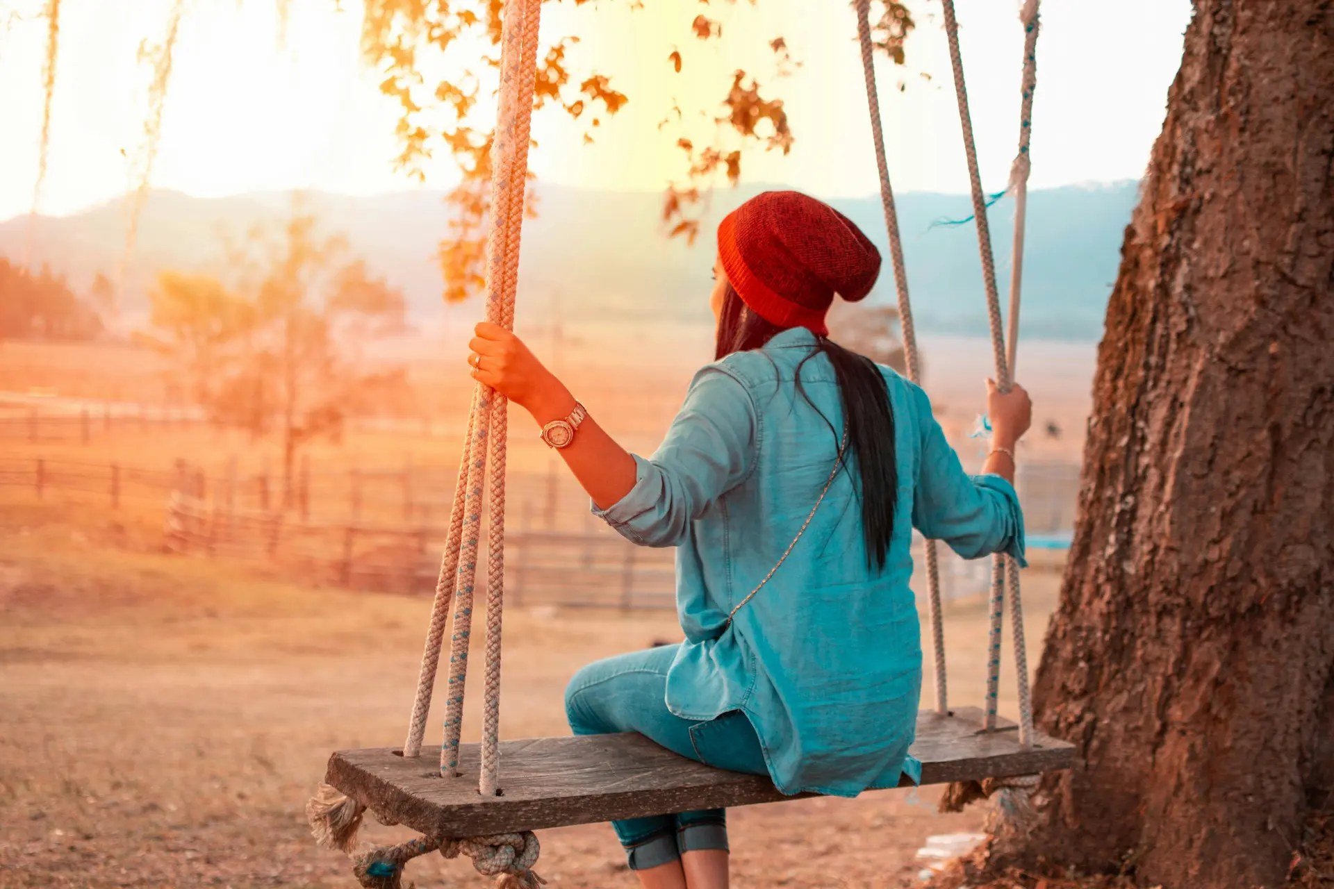 Mujer sentada en un columpio al atardecer, mirando al horizonte con tranquilidad y luz cálida de fondo