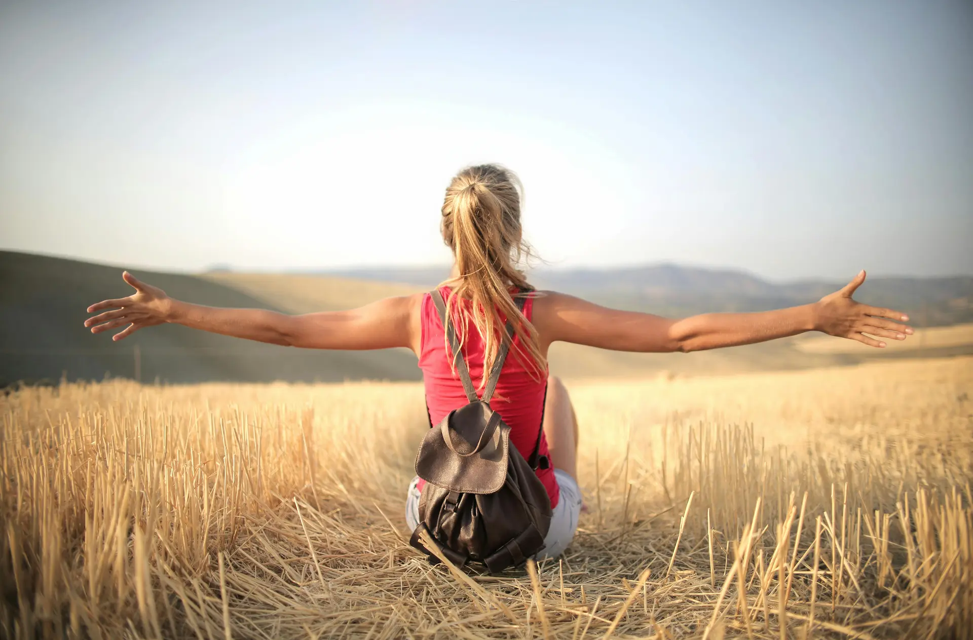 Chica sentada en un campo de trigo con los brazos abiertos, en calma y mirando al horizonte