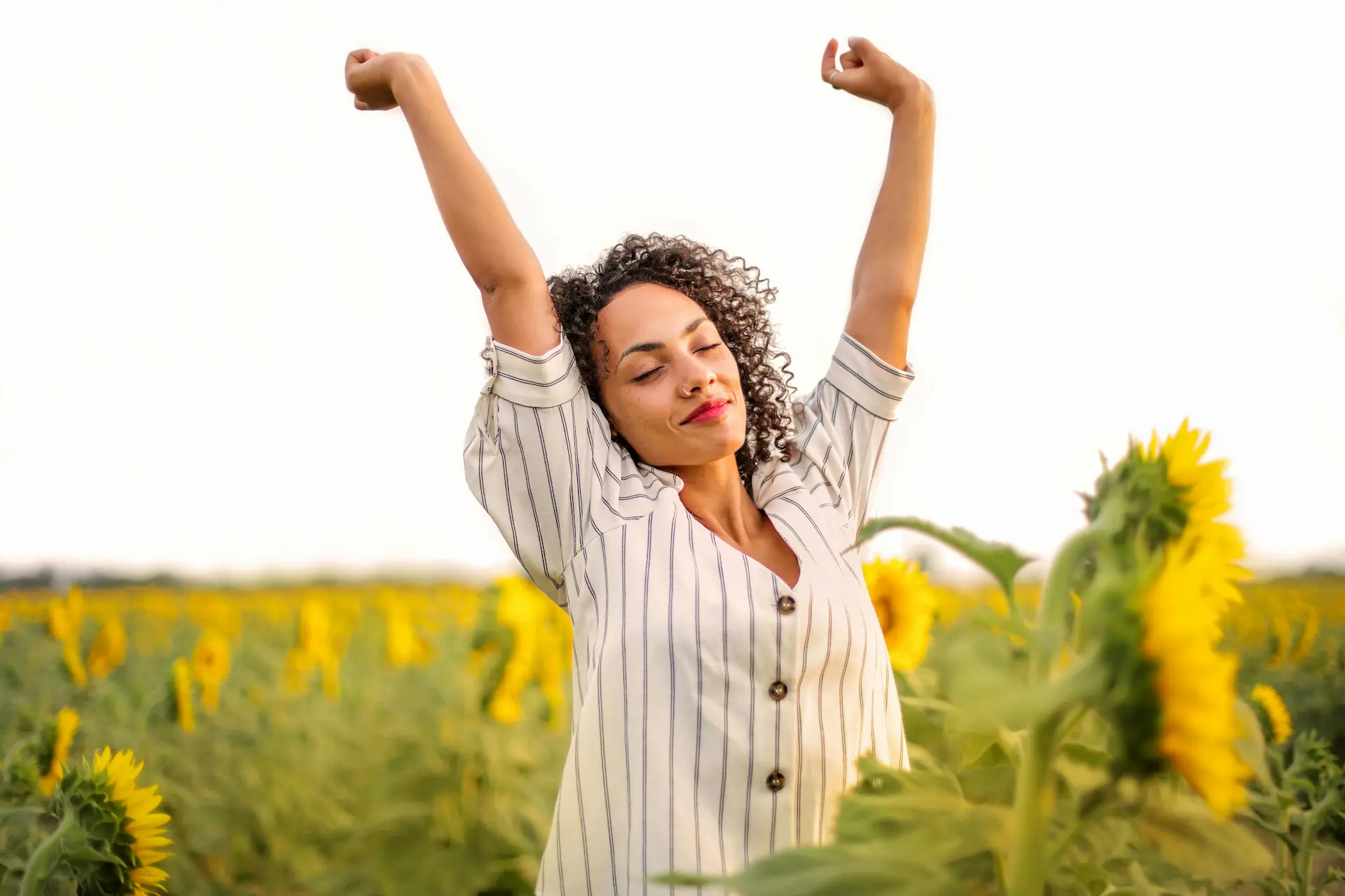 Mujer feliz con los brazos en alto en un campo soleado, simbolizando bienestar tras una terapia individual online