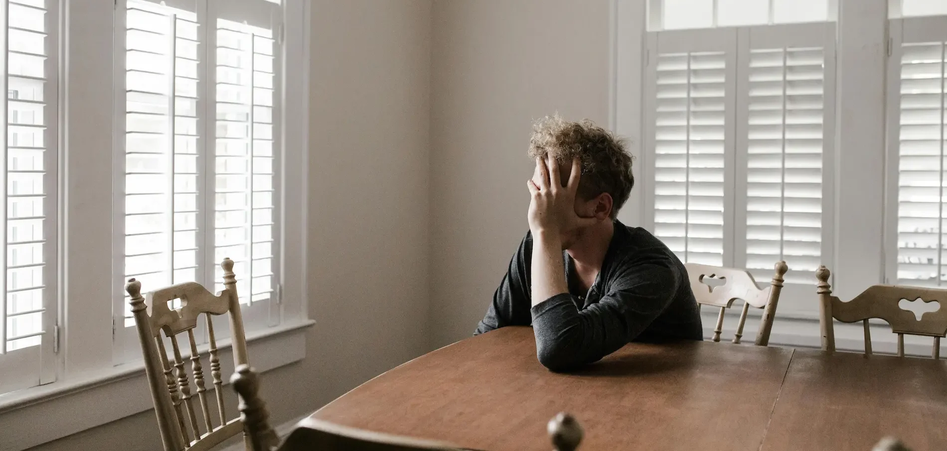 Hombre sentado con las manos en la cabeza en una habitación vacía, en actitud pensativa, representando ansiedad y preocupación