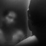 Joven mirándose al espejo con el reflejo difuminado, simbolizando el trauma invisible y la desconexión entre cuerpo y mente
