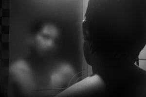 Joven mirándose al espejo con el reflejo difuminado, simbolizando el trauma invisible y la desconexión entre cuerpo y mente