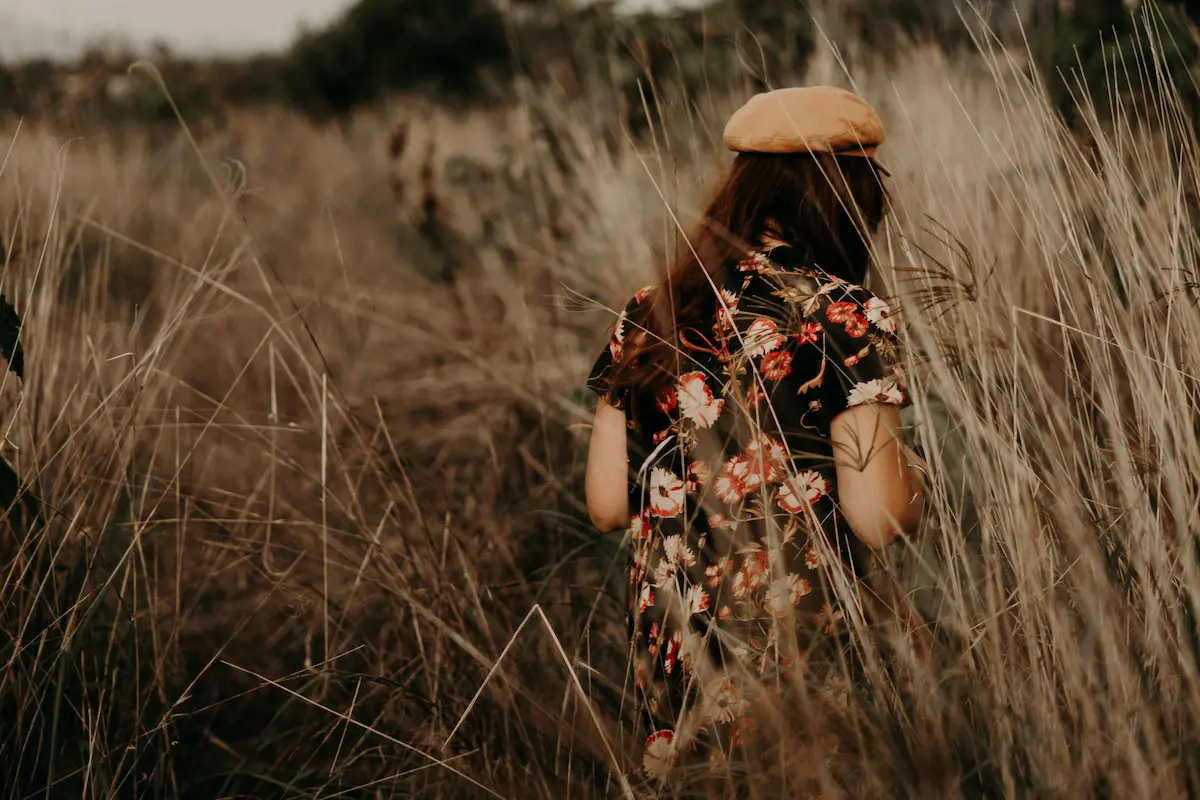 Chica caminando por un campo de trigo al atardecer, simbolizando calma y libertad tras superar la sobreexigencia